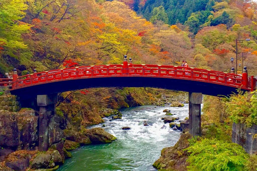 Red Shinkyo Bridge over the river amid autumn foliage in Nikko