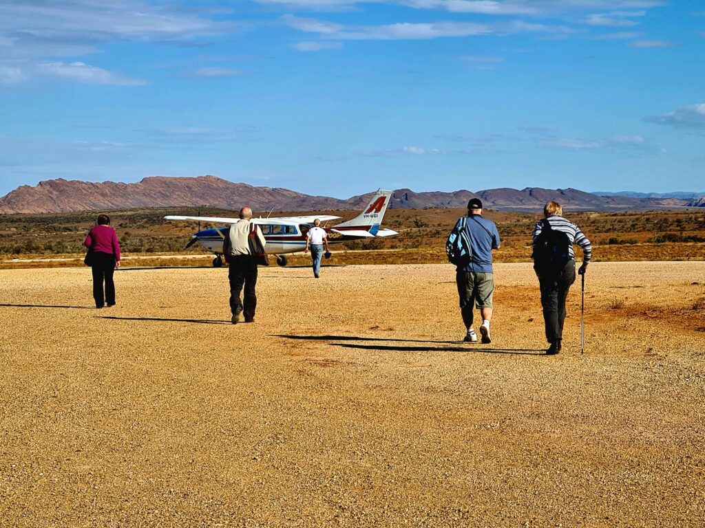 Travellers walking towards a small aircraft with the northern Flinders Ranges behind them