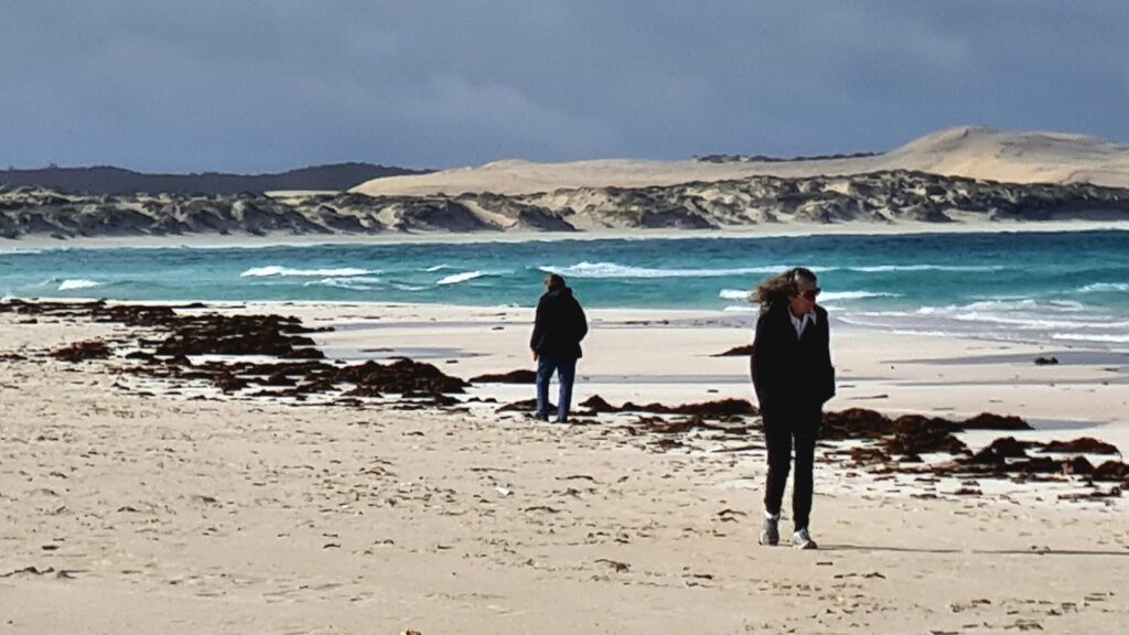 Travellers walking along a white beach beside turquoise water and coastal dunes